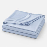 Couverture rafraîchissante Marea bleu poudré, légère et respirante, en tissu effet soie glacée, présentée pliée sur fond blanc.